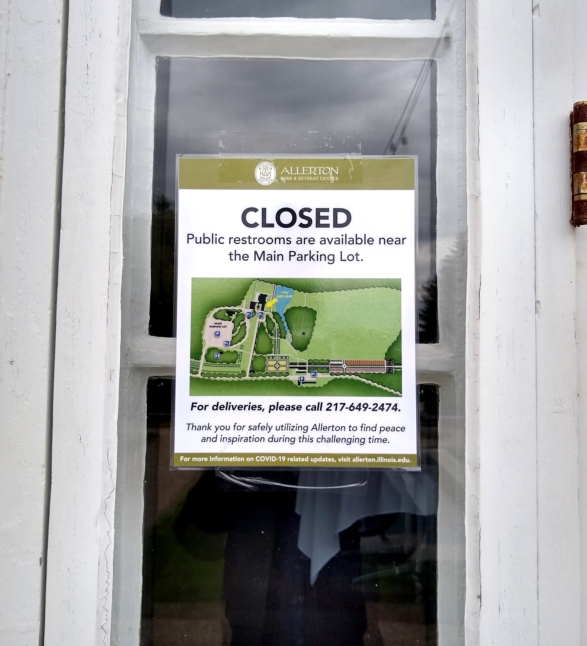 Glasstür mit einem Schild "Geschlossene öffentliche Toiletten verfügbar in der Nähe des Hauptparkplatzes" und einem unklaren Objekt auf der rechten Seite.