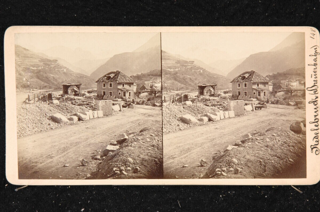 Schwarz-weiß-Foto einer Schotterstraße mit Häusern, Felsen und Bergen im Hintergrund, mit Text auf der rechten Seite.