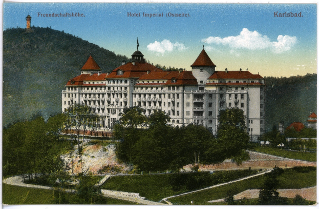 Alte Ansichtskarte des Hotels Imperial in Karlsbad, Deutschland, zeigt ein großes Gebäude mit Fenstern, umgeben von Bäumen, Pflanzen, Gras, einem Pfad, einer Baumgruppe, Hügeln und einem bewölkten Himmel, mit Text oben.