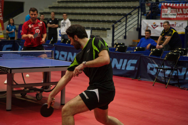 Eine Gruppe von Menschen in verschiedenen Farben, darunter schwarz, weiß und blau, sitzt um einen Tisch mit einem Spiel im Hintergrund, mit Stühlen und einer Treppe.