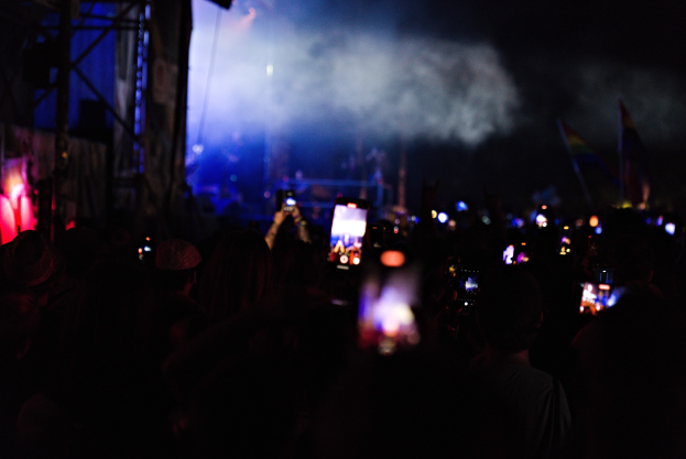 Menge bei einem Konzert mit beleuchteten Handys und Bühnenlicht sowie Rauch im Hintergrund.