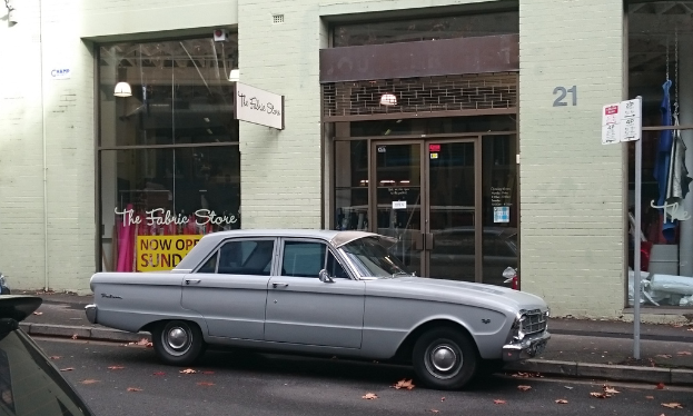 Ein silberfarbenes Auto steht auf der Straße vor einem Gebäude mit mehreren Türen, und an einem Pfahl in der Nähe ist ein Schild mit einer Aufschrift befestigt.