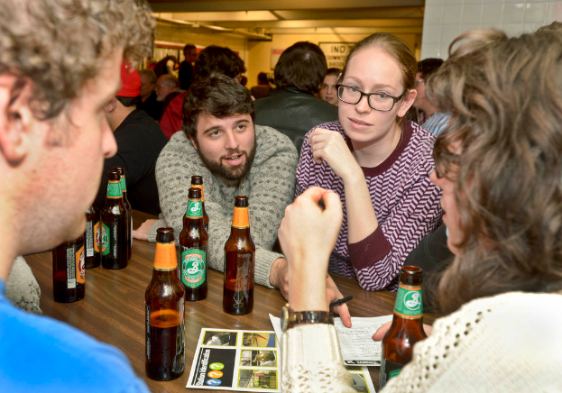 Mehrere Personen auf beiden Seiten eines Tisches mit Bierflaschen in einer Art Bar.