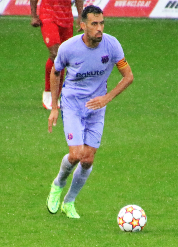 Ein Fußballspieler in einem Sportoutfit und -schuhen ist im Einsatz auf dem Feld, mit einer Tafel mit Text im Hintergrund.