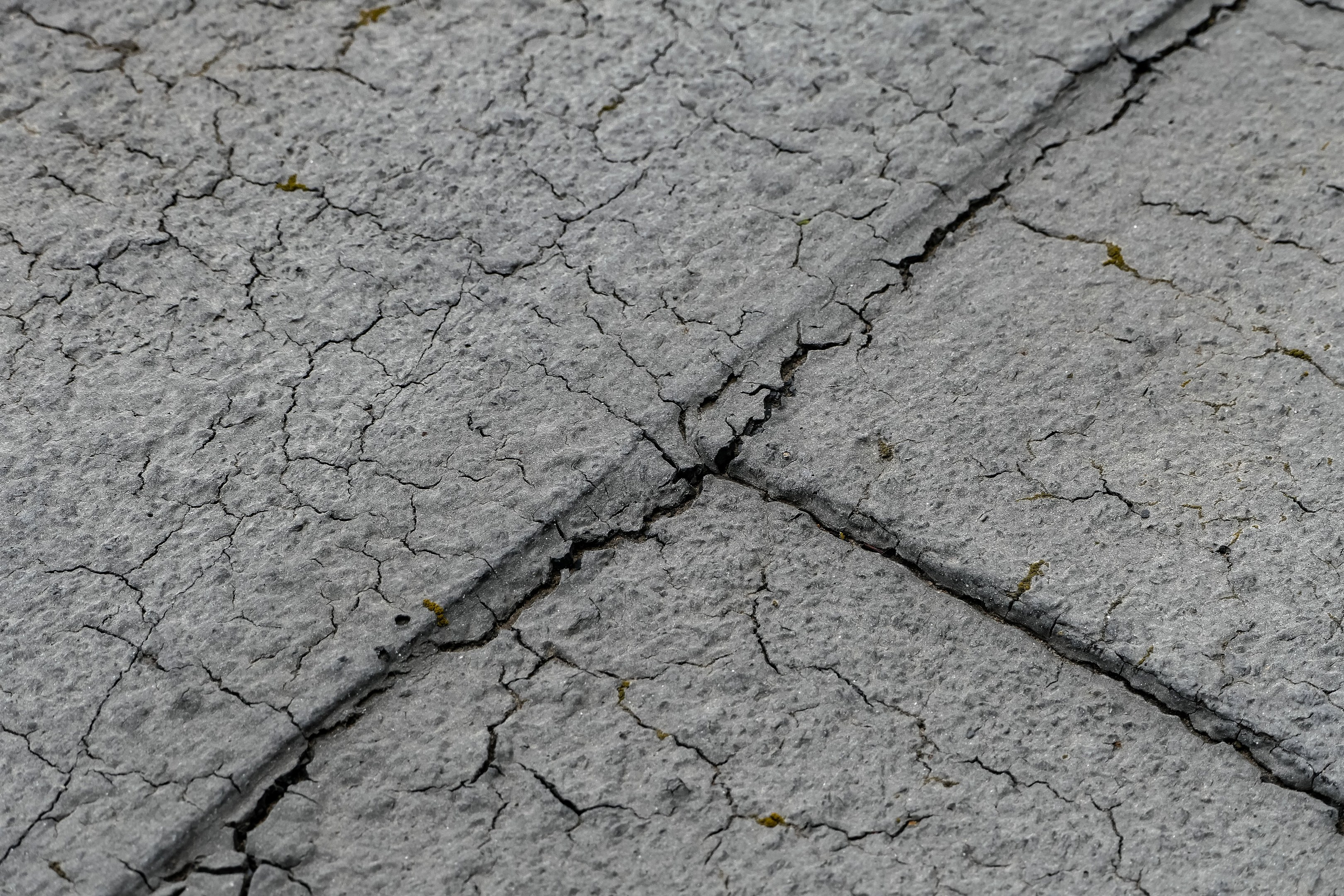 Nahaufnahme einer gebrochenen und verwitterten Straßenoberfläche mit tiefen, breiten Rissen und rauer, unebener Textur.