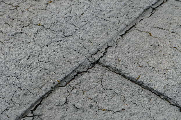 Nahaufnahme einer gebrochenen und verwitterten Straßenoberfläche mit tiefen, breiten Rissen und rauer, unebener Textur.