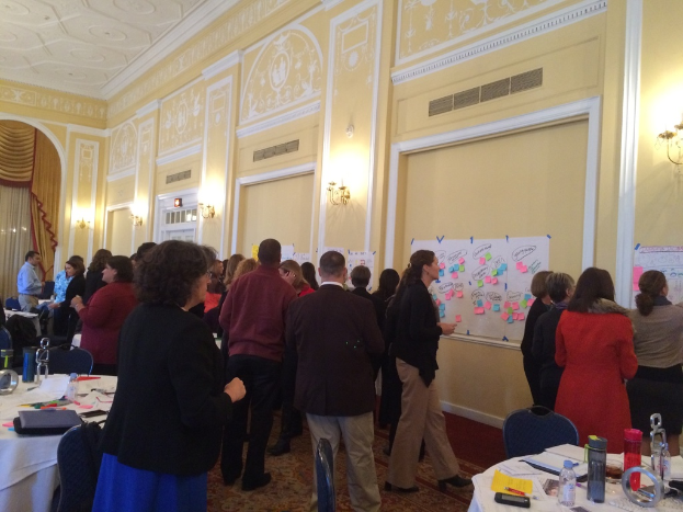 Eine Gruppe von Menschen beobachtet Plakate und Diagramme an einer Wand in einem, was wie ein Kunstmuseum aussieht.