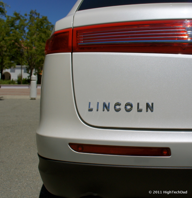 Ein Auto steht neben Zaunpfosten, Bäumen und Gebäuden.