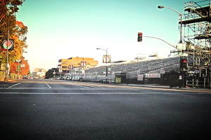 Eine Straße mit einer Ampelstange und Gerät auf der rechten Seite, Warnschilder und mehrere Fahrzeuge vor zahlreichen Bäumen auf der linken Seite.