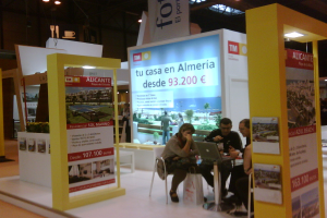 Eine Gruppe von Menschen, die um einen Tisch herum auf Stühlen sitzen und auf einen Laptop schauen, mit mehreren Flyern, auf denen verschiedene Werbeanzeigen zu sehen sind.