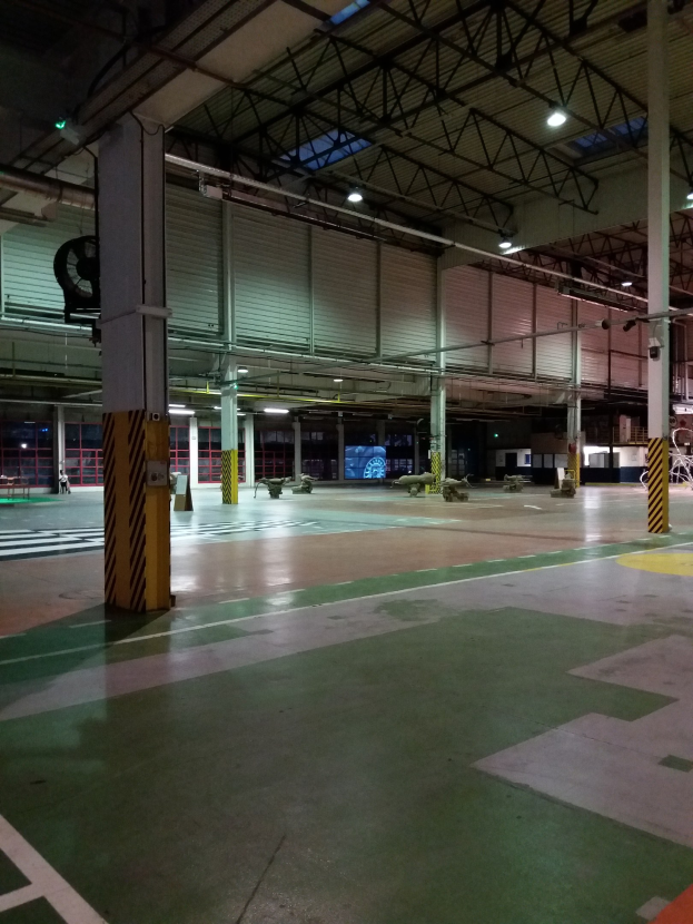 Ein großes Lagerhaus voller verschiedener Maschinen, Metallstangen, Lampen und anderer Gegenstände, mit Text auf dem Boden auf der rechten Seite.