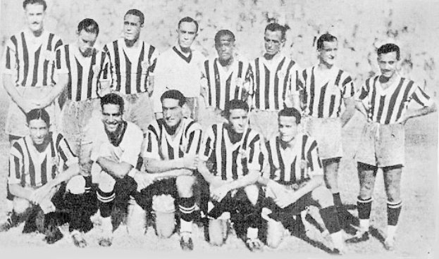 Ein Schwarz-Weiß-Foto einer Fußballmannschaft, wobei einige Spieler stehen und andere auf dem Boden sitzen, mit Text unten.