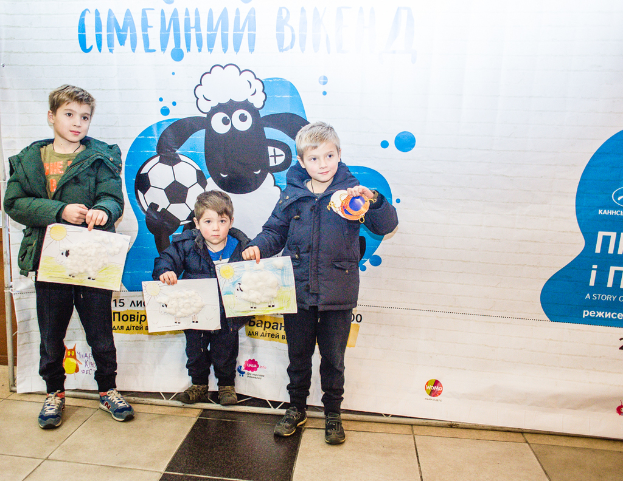 Drei Kinder halten Papiere vor einem Banner.