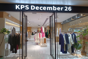 Das Innere eines KPS-Geschäfts am 26. Dezember in Singapur, mit Kleidung an Bügeln, bekleideten Schaufensterpuppen, Topfpflanzen, Glaswänden, Deckenlampen und einem Schild mit Text, wobei der Boden unten zu sehen ist.