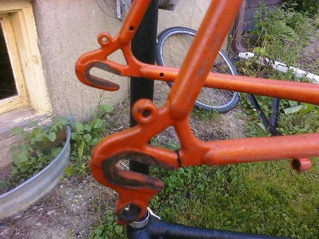 Ein hervorgehobener metallischer Gegenstand auf dem Boden umgeben von verschiedenen Gegenständen, einschließlich eines Rades, anderer metallischer Gegenstände, einer Wand, einer Tür, Pflanzen und Gras.