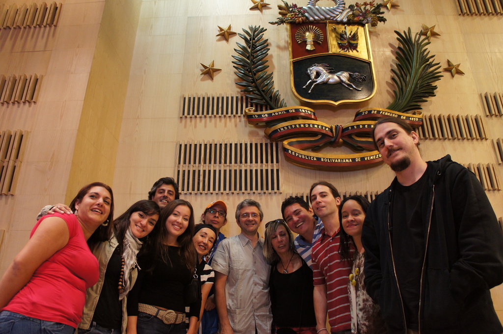 Eine Gruppe lachender Männer und Frauen vor einer Wand mit einem Symbol, Pflanzen und einer Sternenstatue.