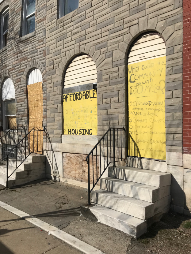 Ein Gebäude mit vernagelten Fenstern und einer Tafel, auf der "Bezahlbarer Wohnraum" steht, mit einer Treppe, die hinaufführt, und einer Straße im Vordergrund.