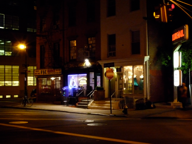 Eine Stadtstraßenszene mit Gebäuden, Geschäften, Bäumen, einer Straße, einem Fahrrad, Treppen und einer Ampel, alles von Lichtern beleuchtet.