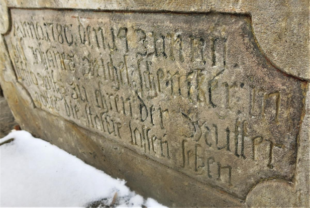 Ein steinernes Schild an einem Gebäude, bedeckt von Schnee, mit Text, der wahrscheinlich Holocaust-Opfern gedenkt.