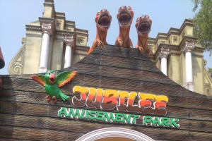 Ein Gebäude mit einem "Jubiläums-Vergnügungspark"-Schild, umgeben von Bäumen unter einem klaren blauen Himmel, mit Tierfiguren auf seinem Dach.