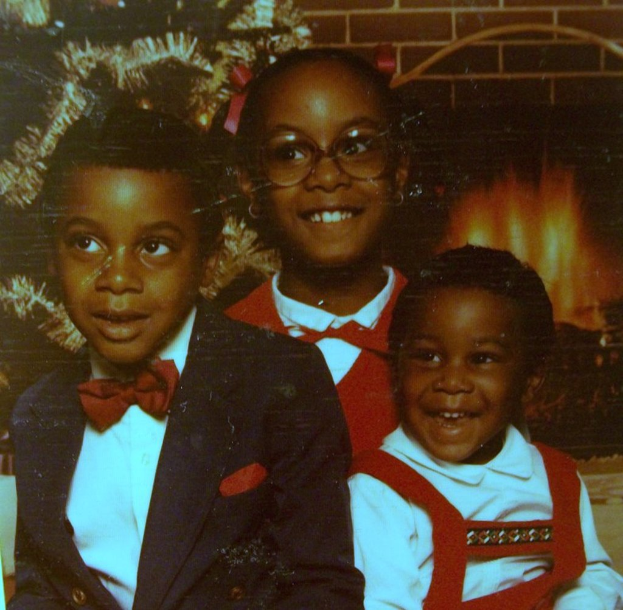 Drei lachende Kinder vor einem Weihnachtsbaum mit Kamin auf der rechten Seite.