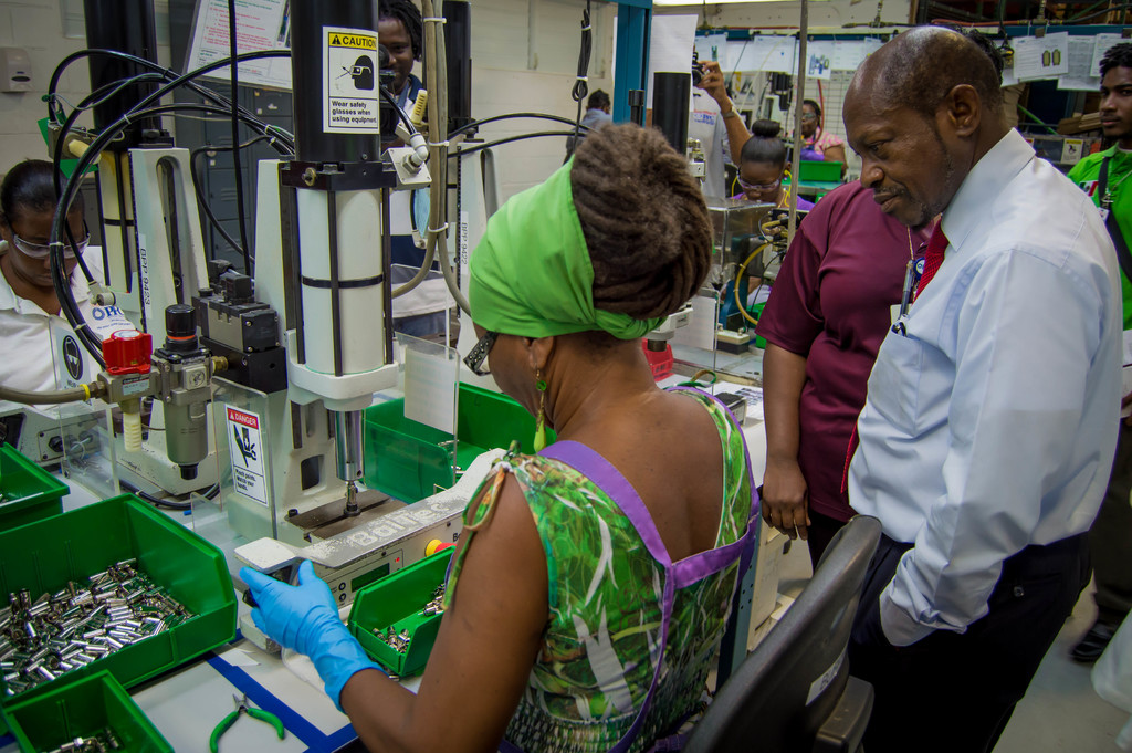 Eine Frau bedient eine Maschine mit einem Warnschild, umgeben von Drähten, Papieren und Gegenständen in einem grünen Behälter.