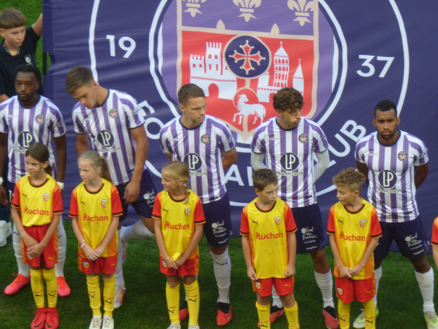 Eine Gruppe junger Menschen auf einem Fußballfeld, mit einem Banner im Hintergrund, auf dem steht "Preston Primary School Football Team".