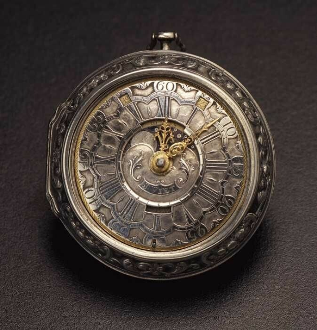 Eine silberne Taschenuhr mit römischen Ziffern auf ihrem Zifferblatt, die auf einer schwarzen Oberfläche ruht und detaillierte Zifferblattmerkmale aufweist, die typisch für eine Londoner Taschenuhr sind.