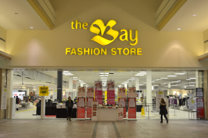 Vorbereitungen im Geschäft eines Bay Fashion Shops in einem Einkaufszentrum mit Kunden, Wandtafeln, Säulen, Deckenleuchten und Hintergrundauslagen.