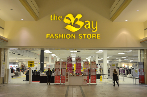 Vorbereitungen im Geschäft eines Bay Fashion Shops in einem Einkaufszentrum mit Kunden, Wandtafeln, Säulen, Deckenleuchten und Hintergrundauslagen.