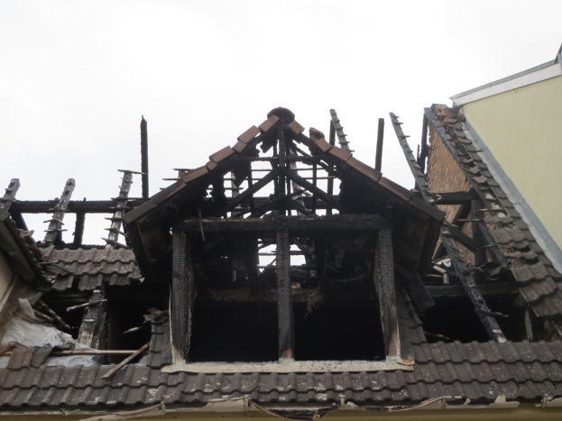 Ein Gebäude mit einem durch Feuer beschädigten Dach, das abgerissen wird, mit herumliegendem Schutt, darunter Holzplanken, vor einem Himmel-Hintergrund.
