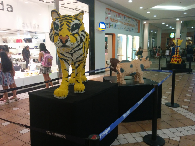 Tierfiguren auf schwarzen Kisten umgeben von Stangen mit Gummibändern, mit Geschäften, die Taschen, Schuhe und andere Artikel anbieten, und Menschen, die herumlaufen.