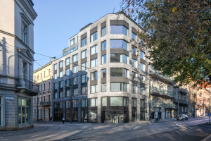 Großes modernes Bürogebäude mit zahlreichen Fenstern, umgeben von Straßeninfrastruktur, Fahrzeugen, Fußgängern, Bäumen und einem bewölkten Himmel.