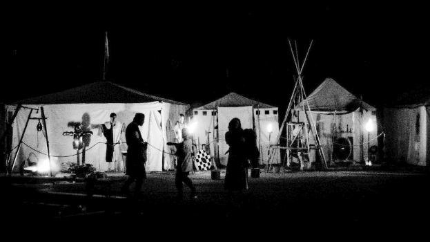 Eine Nachtansicht von beleuchteten Zelten mit Menschen in der Nähe, vor einem dunklen Hintergrund.