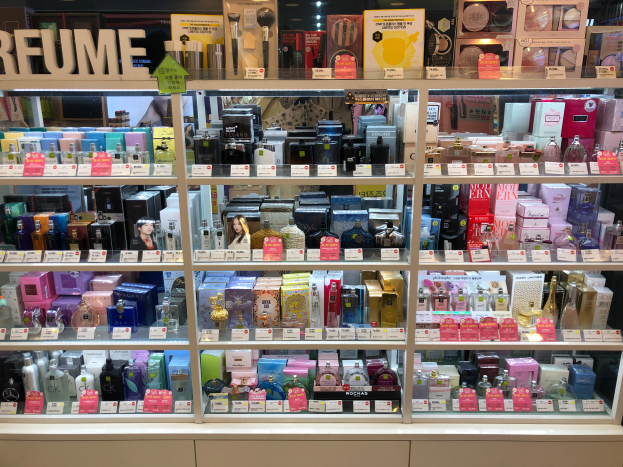 Ein Ausstellungsregal voller verschiedener Parfümflaschen, die in Regalen mit Preisschildern angeordnet sind und von oben beleuchtet werden.