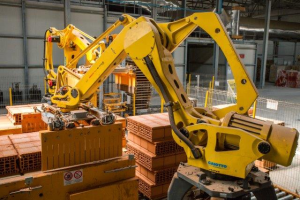 Ein großes Lager mit zahlreichen Kisten, Kränen und diverser Industrieausrüstung, mit einem Zaun und Pfählen im Vordergrund und einer Wand im Hintergrund.