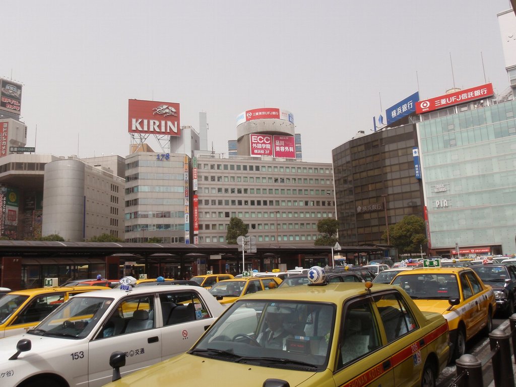 Eine Stadtansicht mit Fahrzeugen auf der Straße, Gebäuden, Bäumen, Pfählen mit Schildern und Text auf den Schildern, einem Zug im Hintergrund und einem Geländer unten rechts.