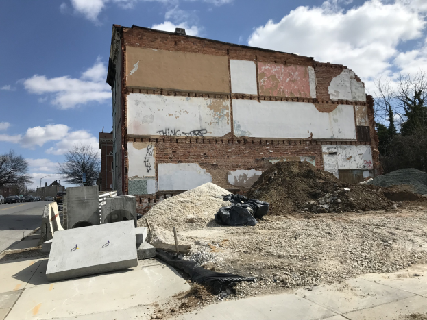 Ein altes, teilweise abgerissenes Gebäude mit Graffiti, umgeben von Fahrzeugen, Bäumen und einem bewölkten Himmel.