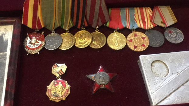 Eine hölzerne Box mit verschiedenen Medaillen, darunter ein roter Stern, mit einem Objekt auf der rechten Seite.