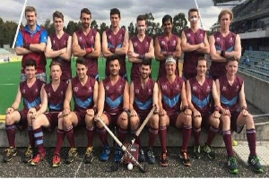Eine Gruppe von Männern, die auf einem Feld mit Hockey-Schlägern feiern, umgeben von Bäumen und einem Stadion.