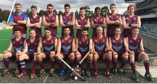 Eine Gruppe von Männern, die auf einem Feld mit Hockey-Schlägern feiern, umgeben von Bäumen und einem Stadion.