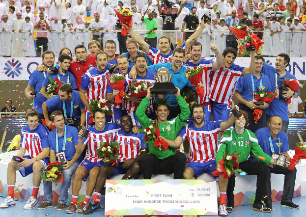 Eine Gruppe von Menschen in Sportbekleidung, einige halten einen Award und Blumen, steht vor einer Menge mit Geländern und Schildern im Hintergrund.