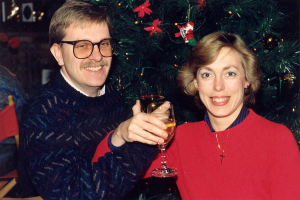 Ein Paar lächelt, während es Gläser Wein hält, mit einem Weihnachtsbaum im Hintergrund.