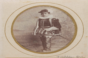 Ein altes Foto eines Mannes in traditioneller schottischer Kleidung, einschließlich eines Kilts, weißem Hemd, schwarzem Weste und schwarzem Hut, der entschlossen mit einem Schwert in der Hand steht.