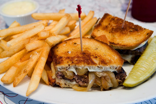 Ein weißer Teller mit Pommes frites, Burgern und einer Schüssel in der oberen linken Ecke.