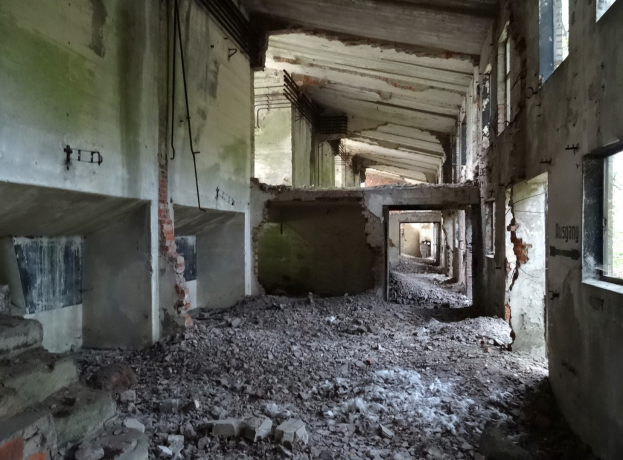 Altes Gebäude mit erheblichen strukturellen Schäden, darunter eingestürzte Wände, zerbrochene Fenster, freiliegende Rohre und verstreute Trümmmer.