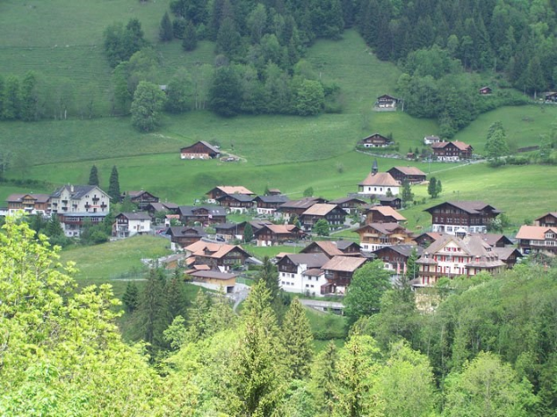 Kleines Dorf mit bunten Häusern umgeben von grünen Bäumen und Gras in einem Tal.