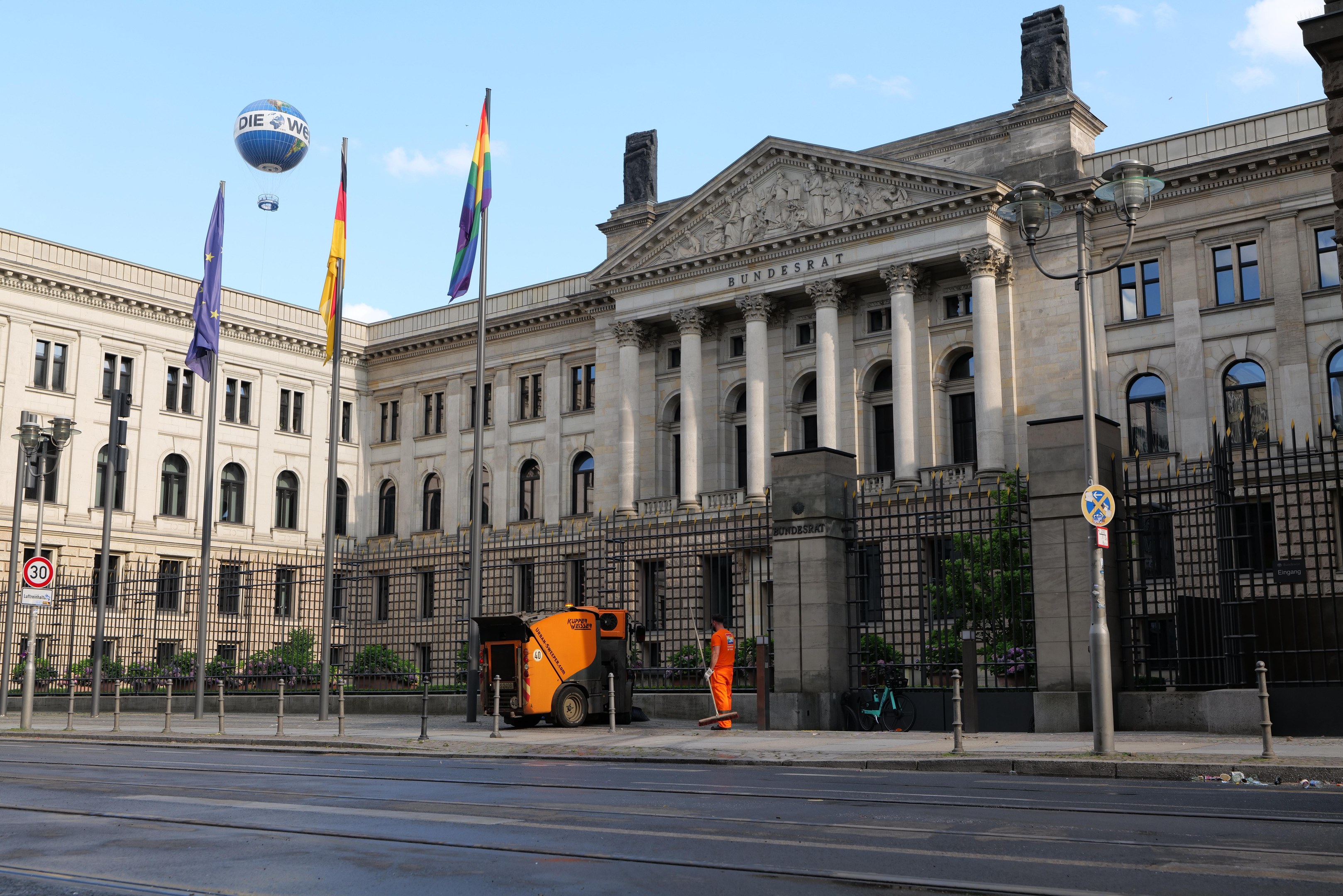 Großes beiges Gebäude mit vielen Fenstern, beschriftet mit "Bundestag", umgeben von Straßeninfrastruktur und Fußgängern, unter einem bewölkten Himmel.
