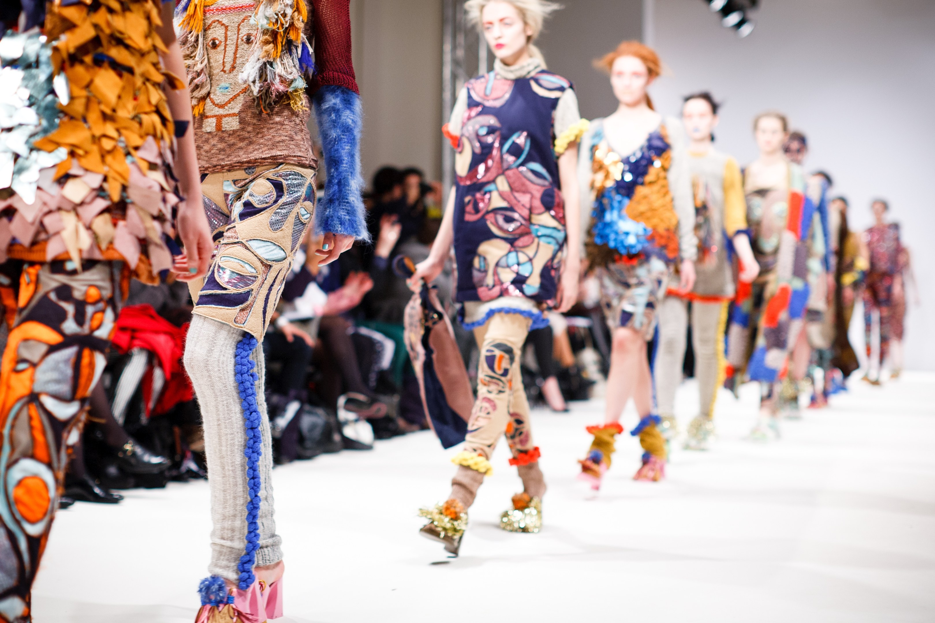Eine Gruppe von Frauen, die auf dem London Fashion Week Laufsteg geht, mit sitzenden Zuschauern und heller Beleuchtung im Hintergrund, die einen traumhaften Effekt schafft.
