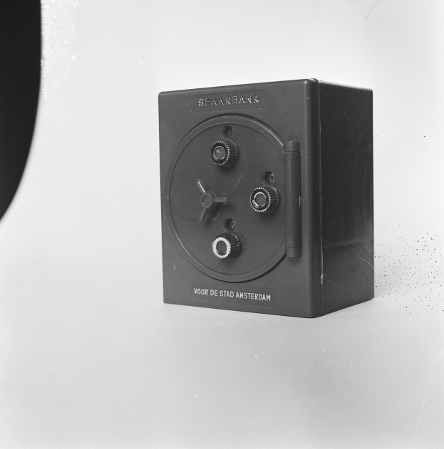 Ein Schwarz-Weiß-Foto eines rechteckigen Sicherheitsschranks auf einer weißen Oberfläche, mit einem Griff oben, einem Schloss vorne und einem Schlüsselloch in der Mitte.